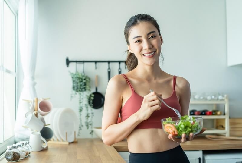 Asian woman eating bowl of salad