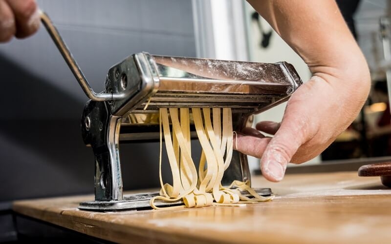 Chef rolling dough with a pasta machine. Pasta maker machine.