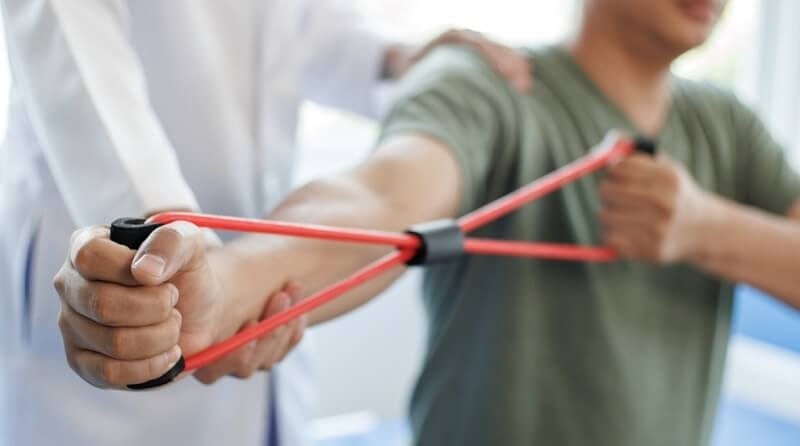 doctor helping patient doing exercises with resistant band 