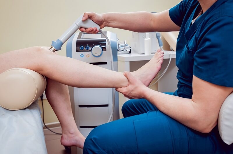 Doctor doing Shock wave therapy on patients leg, Physiotherapy rehabilitation 