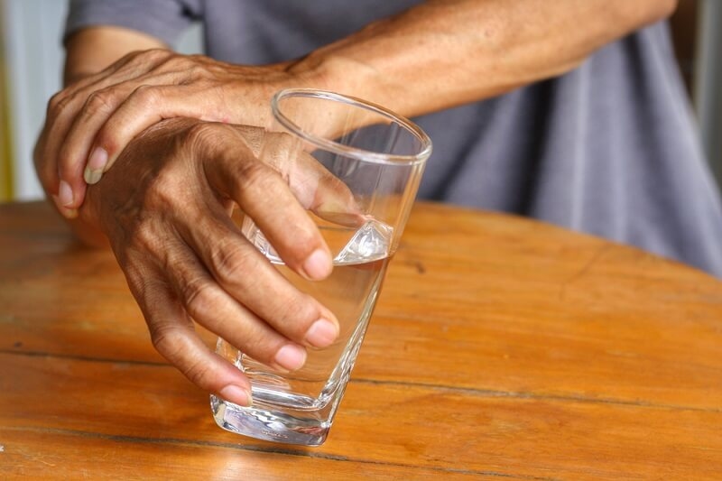 Elderly man having trouble holding glass of water because of Tremor