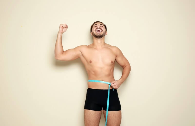 Fit man measuring his waist happy about weight loss