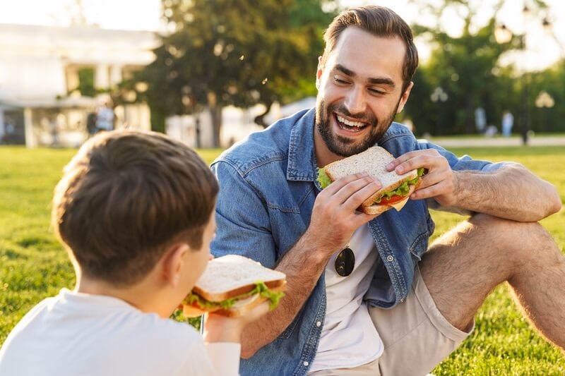 Happy father eating sandwiches with his son