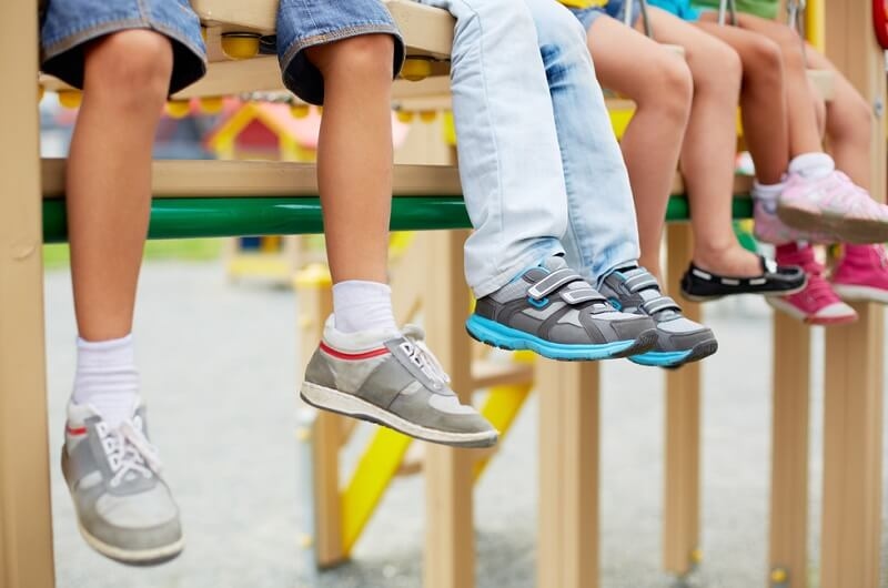 Legs wearing shoes of little kids sitting on swing