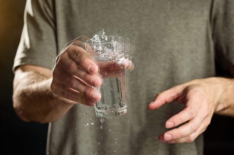 Man with Parkinson's disease holds a glass of water with a shaking hand