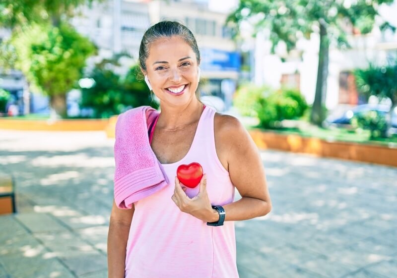 Middle age sportswoman holding heart shape model in the park