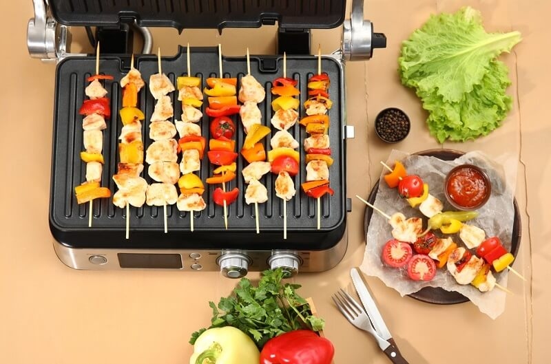 Modern electric grill with tasty chicken skewers and vegetables