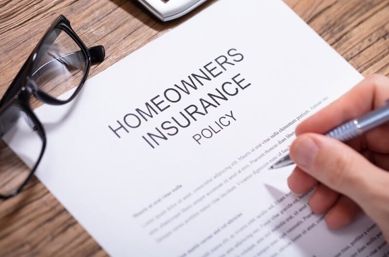 Person's Hand Filling Homeowners Insurance Policy Form on Wooden Desk