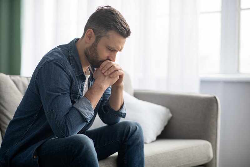 Sad bearded middle-aged man sitting on couch at home