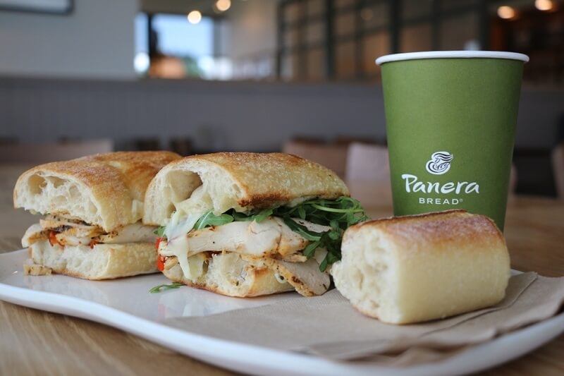 Sandwich and Green paper drinking cup with Panera Bread logo on a table