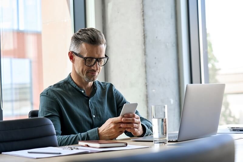 Smiling mature businessman holding smartphone sitting in office