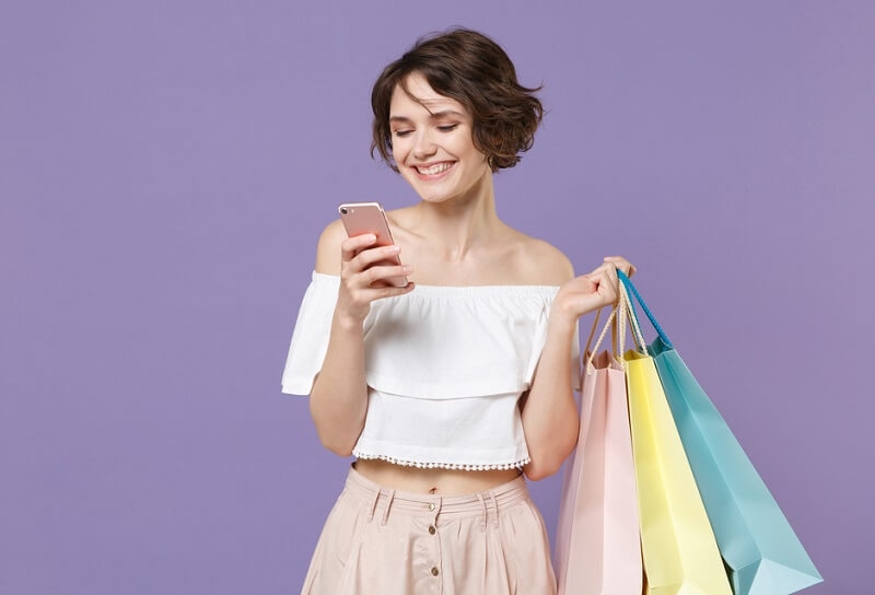 Smiling woman holding shopping bag and looking at her smartphone