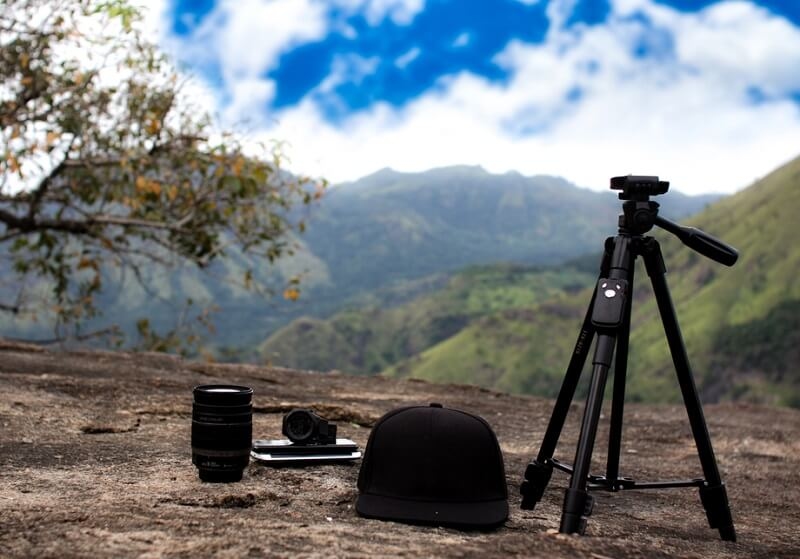 Tripod, lense, hat laying on ground. mountain in background