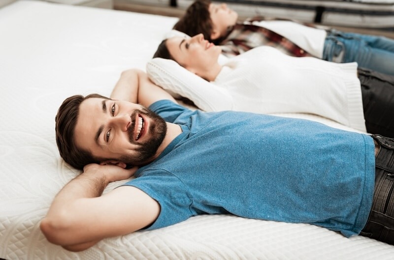 happy couple with little boy lies on bed in mattress store