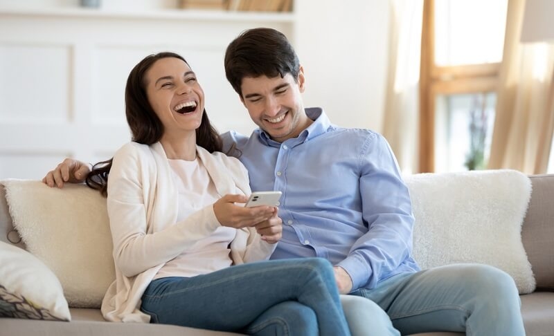 couple laughing, having fun sitting on sofa