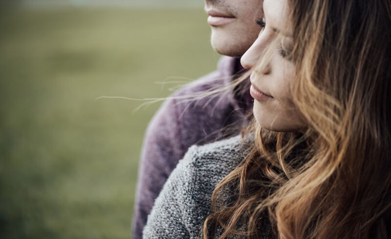 couple outdoors sitting on grass, hugging and looking away