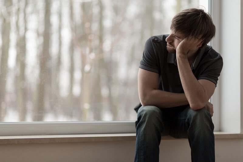 depressed man sitting and thinking near window