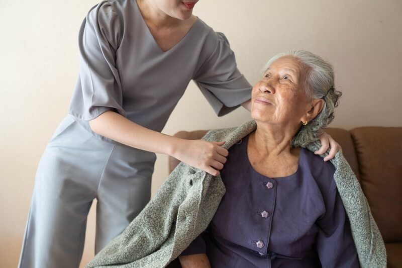 female nurse covering elderly patient with sweater