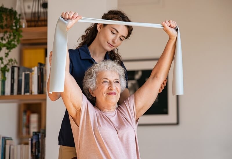 female physiotherapist helping senior woman with resistance band