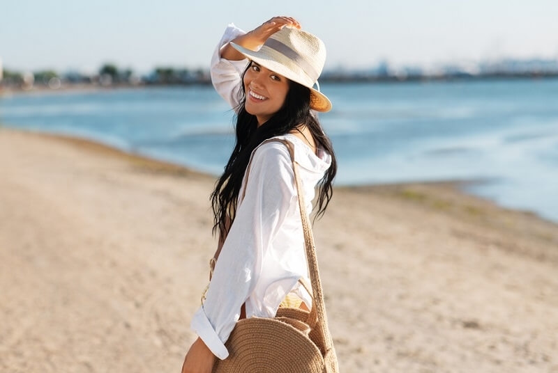 happy smiling woman in white shirt and straw hat walking along beach