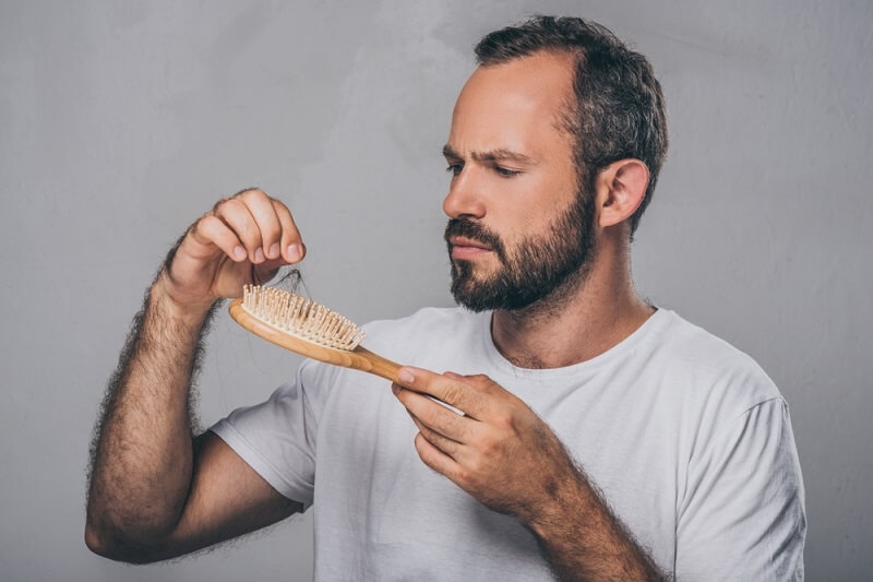 man picking hair from hairbrush. Hair loss concept