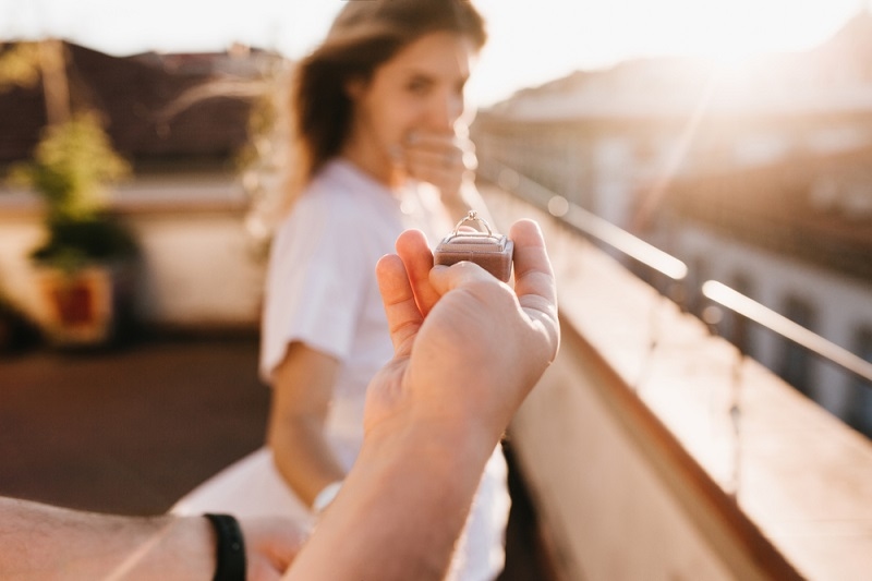 Man holding engagement ring in front of astonished happy girl