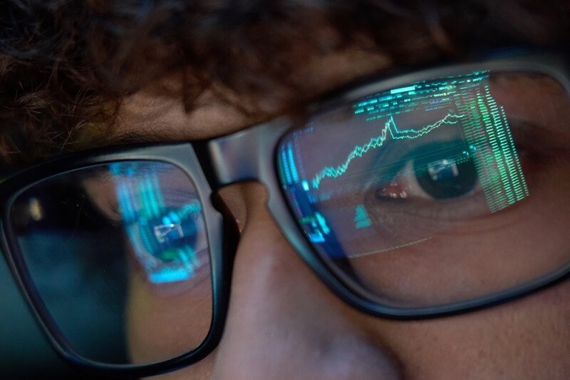 man trader wearing glasses looking at computer screen with trading charts reflecting in eyeglasses