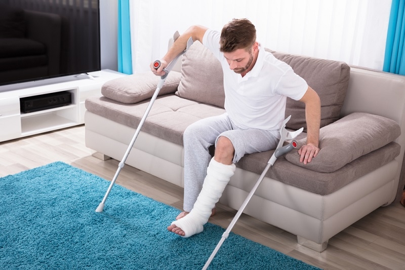 Young Man With Broken left Leg trying to get up from sofa