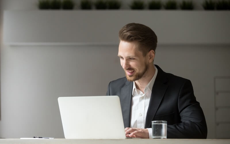 man working online on laptop sitting in suit at office desk