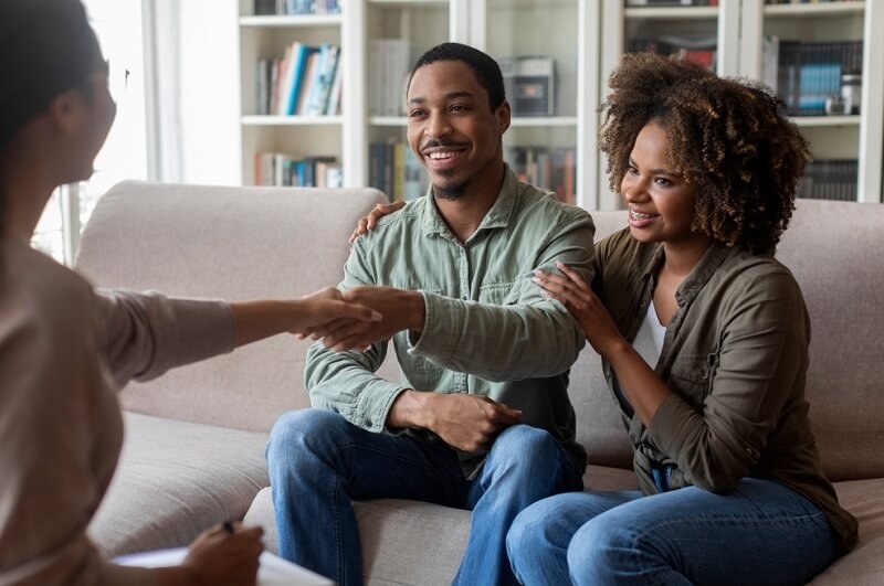 smiling african american couple talking with female therapist shaking hands