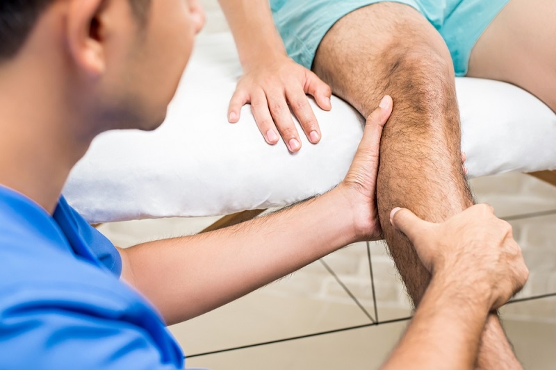 Therapist treating male patient knee pain in clinic