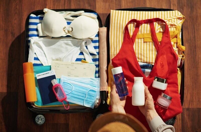 woman adding beauty and health products on her suitcase