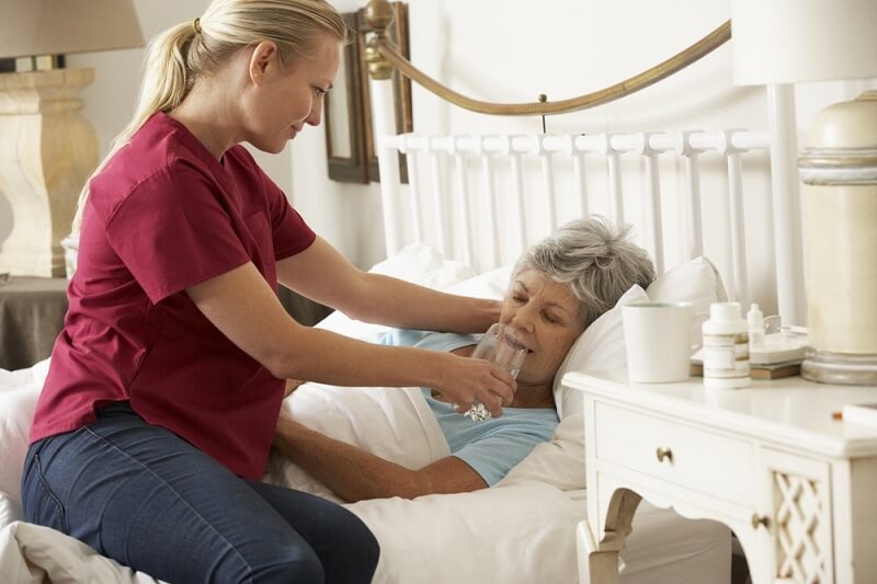 woman helping elderly patient drink a glass Of Water In Bed