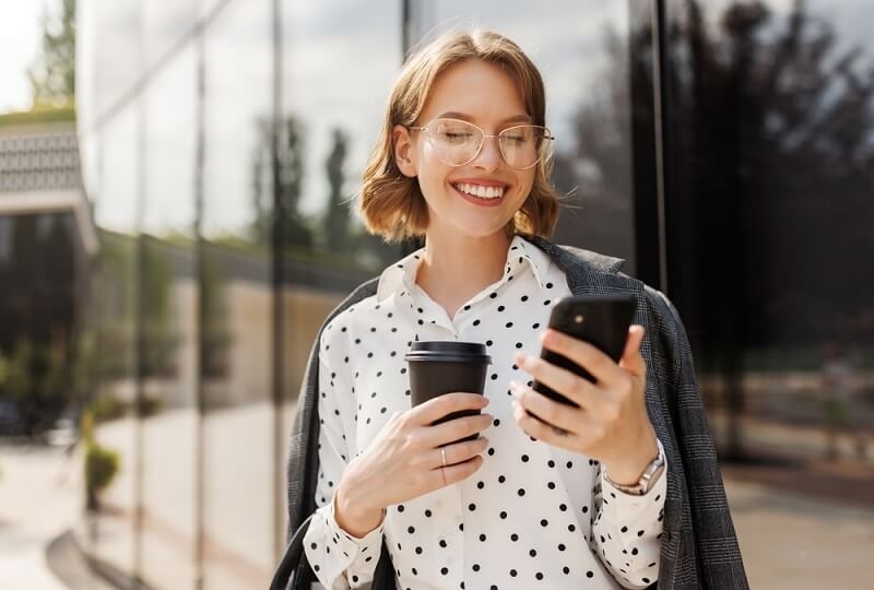 woman holding coffee cup in hand and using mobile phone