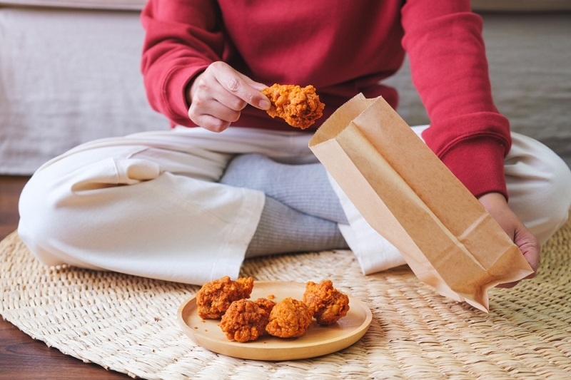 woman picking fried chicken from paper food bag