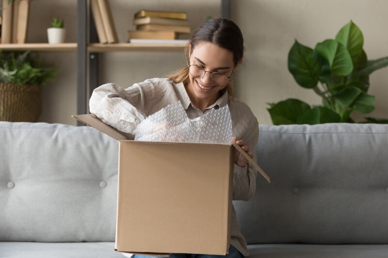 woman sitting on sofa unpacking online delivery package