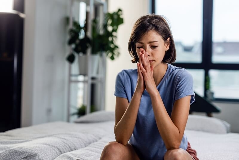 woman with hands clasped sitting on the bed and thinking