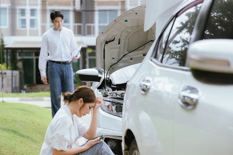 woman sitting on ground after accident and inspecting officer checking car