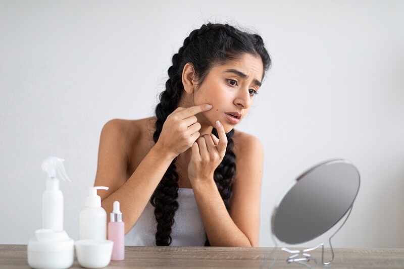 woman looking at the acne in mirror