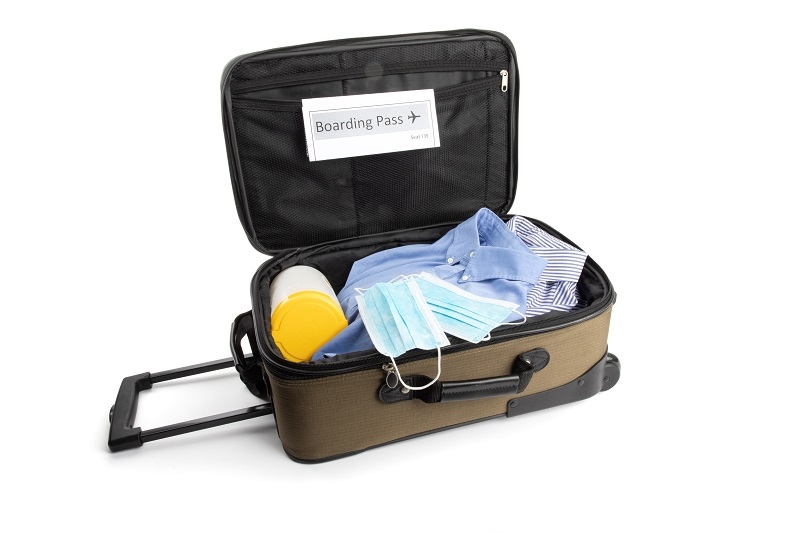 a carry on suitcase with a generic boarding pass, a surgical mask and disinfecting wipes