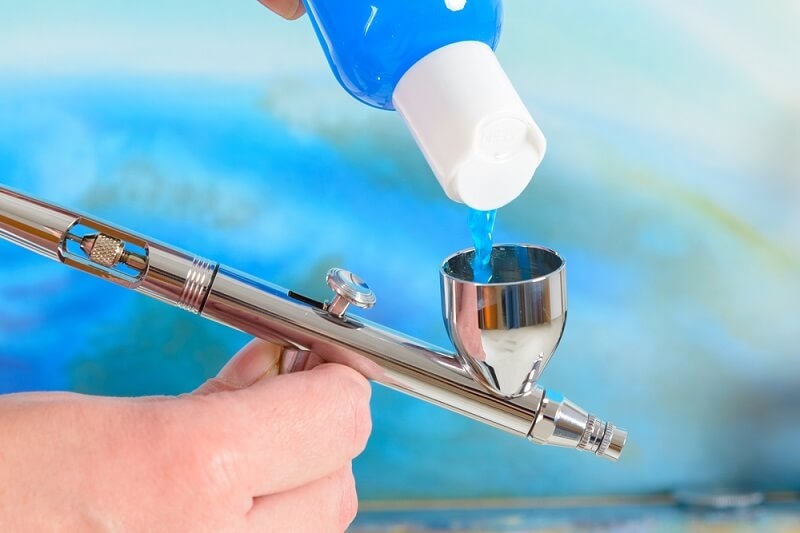 man filling airbrush gun with paint color'