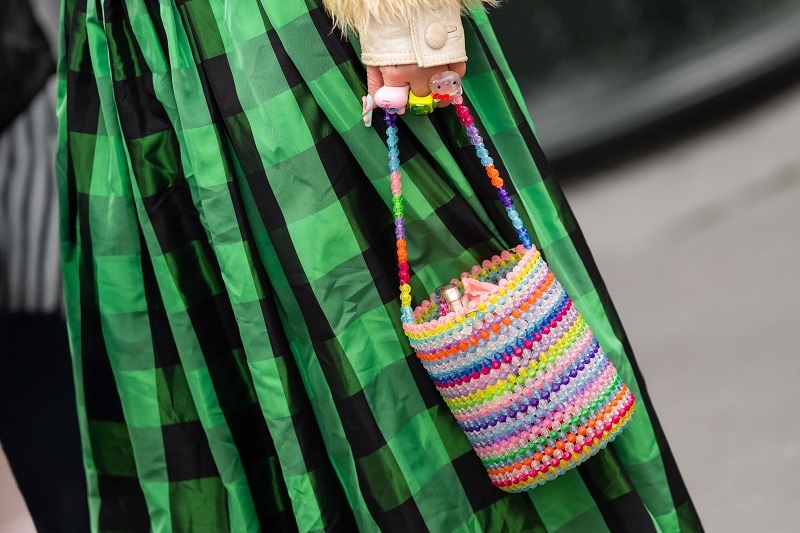 Rainbow beaded bucket bag with toys and colorful rings, worn with green check pleated midi skirt