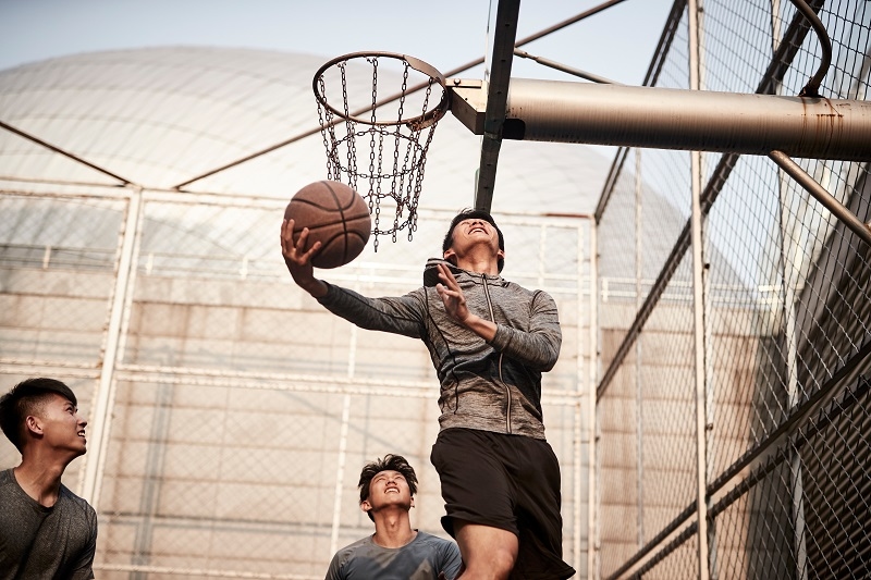 young asian adult men playing basketball on outdoor court