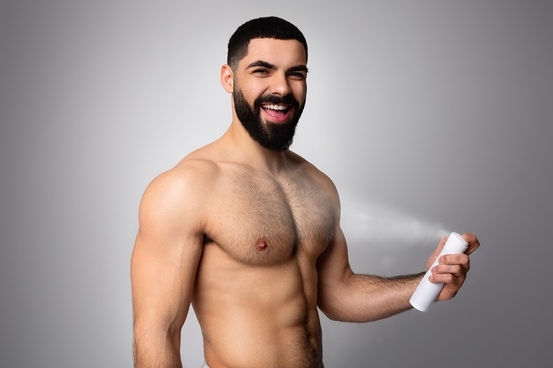 Shirtless young bearded middle eastern man using deodorant spray