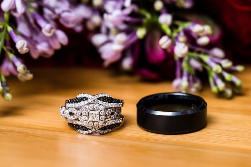 two different material wedding bands on table with flowers 
