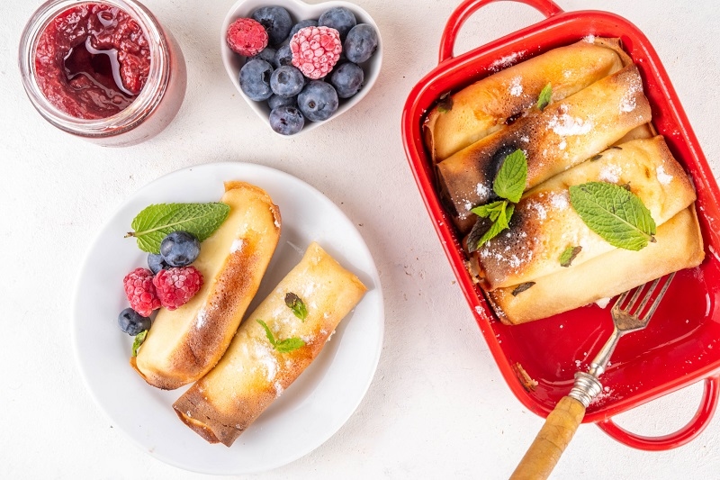 Traditional German Pfannkuchen-Auflauf, baked pancakes casserole. Sweet dessert casserole for breakfast made with thin pancake crepes with cream cheese, with fresh berry and powdered sugar