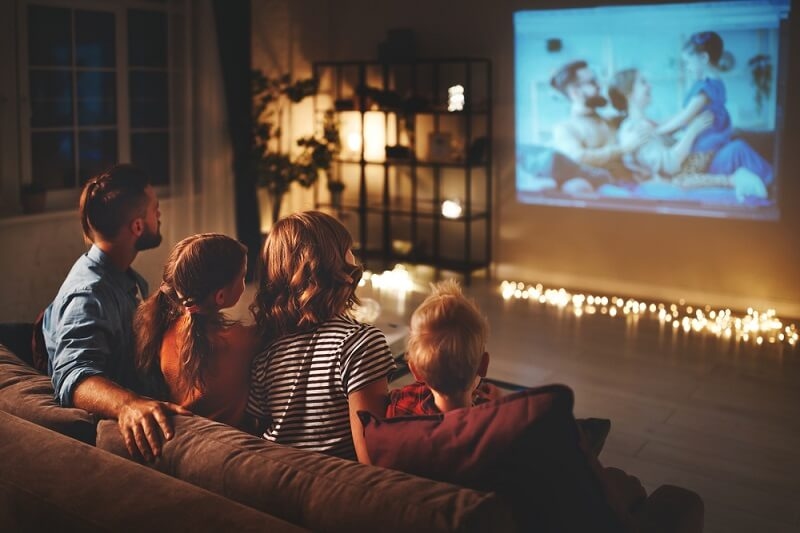 family sitting on sofa and watching movie on home projector 