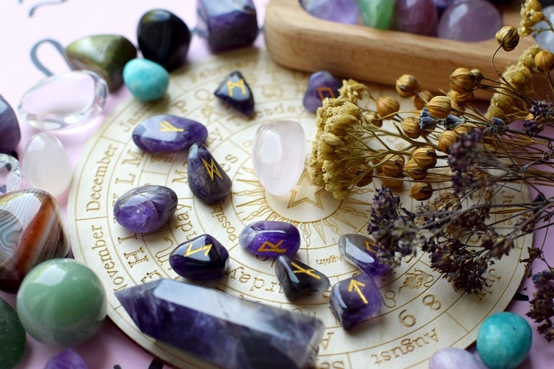amethyst and dry herbs on a pink background with a board with symbols of the zodiac signs