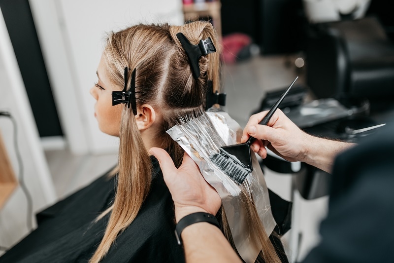 Hairdresser is applying bleaching powder on woman's hair and wrapping into the foil. 