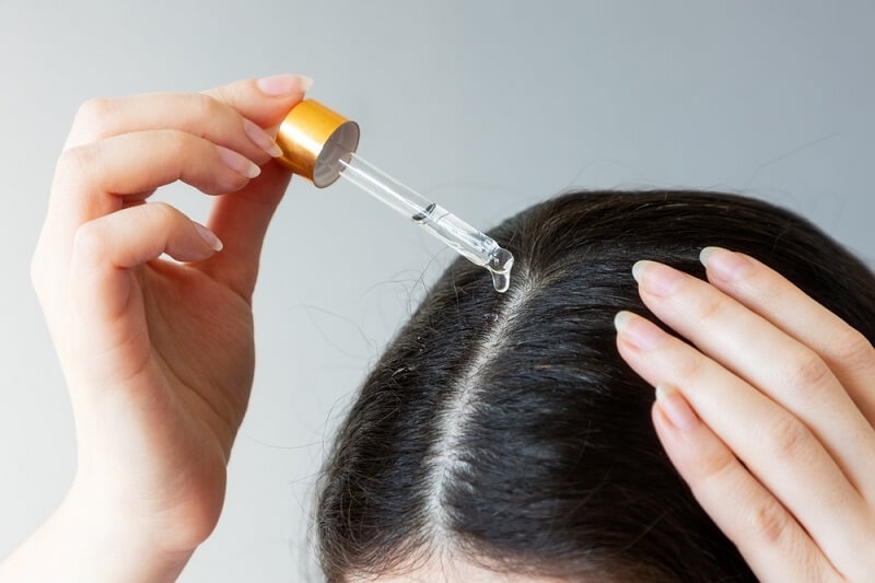 woman applying hair growth serum with vitamin with dropper
